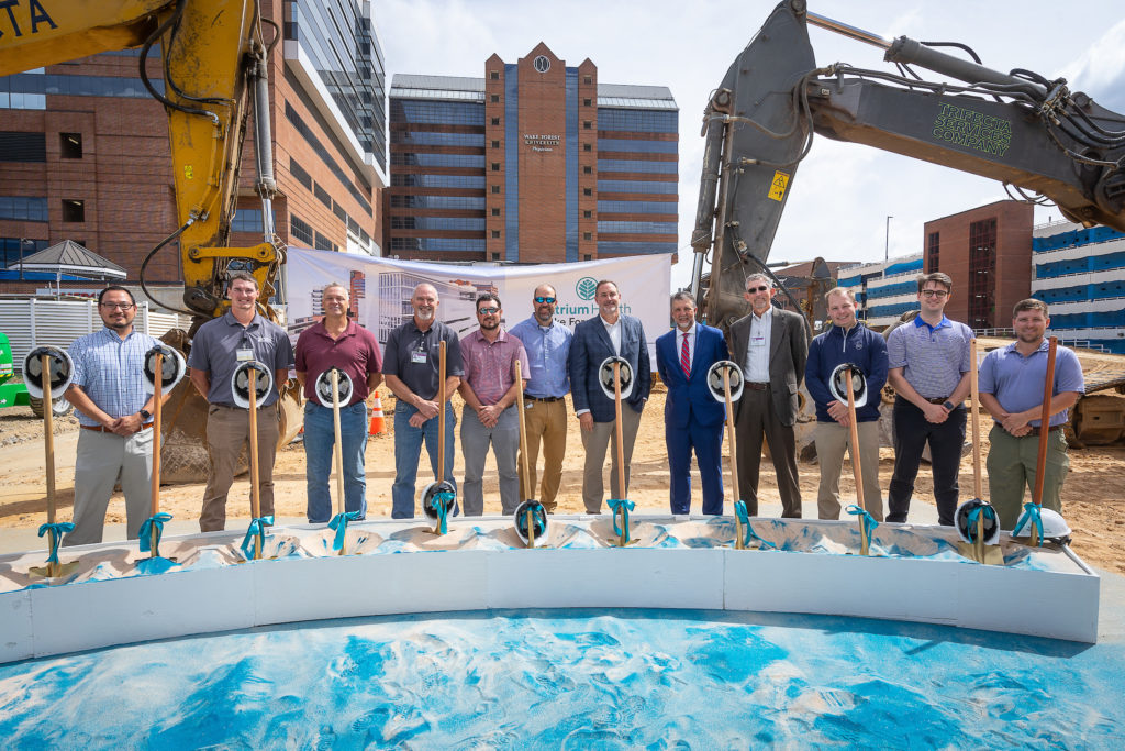 A dozen people stand behind shovels at a construction groundbreaking event
