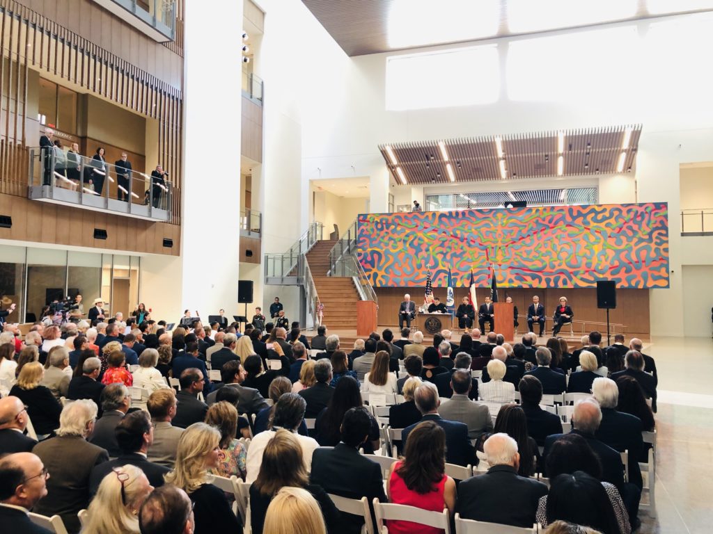 a vibrant mural serves as a visual focal point for a courthouse atrium. a crowd of people gather for the grand opening with the mural in the background