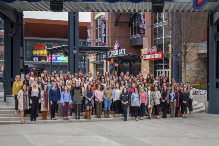 Group of people from the Women's Operational Resource Group posing for a photo at an outdoor venue with eateries and an entrance gate in the background, radiating camaraderie.