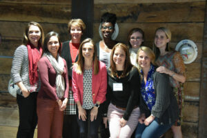 Group of eight women from the Women's Operational Resource Group showcasing camaraderie while posing for a photo with a wooden wall as the backdrop.