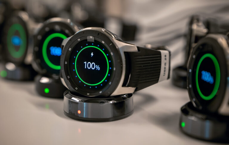 Smartwatches on charging docks displaying 100% battery level.