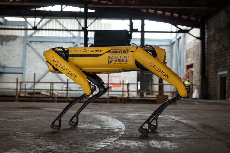 A Boston Dynamics quadruped robot in an industrial setting, marked with caution tape and the warning