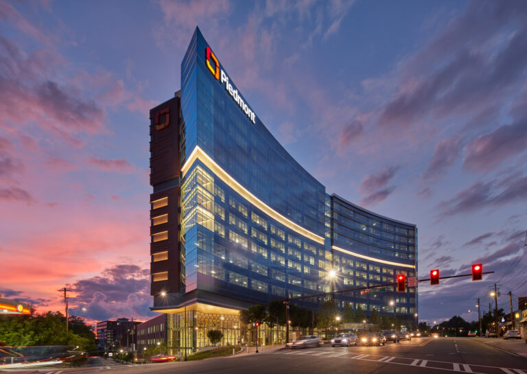 Modern corporate office building at twilight with illuminated windows and street traffic lights, featured in a leading Construction Industry publication.