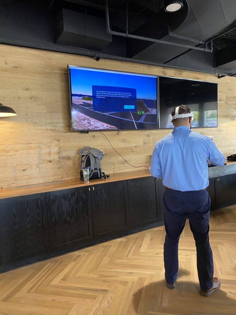 Man using a virtual reality headset facing two large screens displaying digital content for BIM and construction project site awareness.