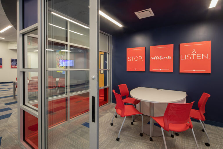 Modern meeting room in the renovated Jackson Preparatory School with red chairs, a white round table, and motivational artwork on blue walls.