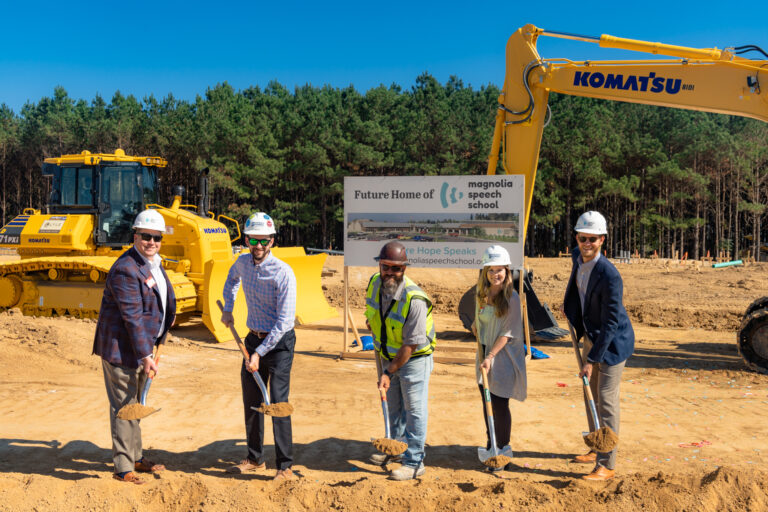 Group of individuals at a groundbreaking ceremony for the new Magnolia Speech School in Mississippi, with construction equipment in the background.
