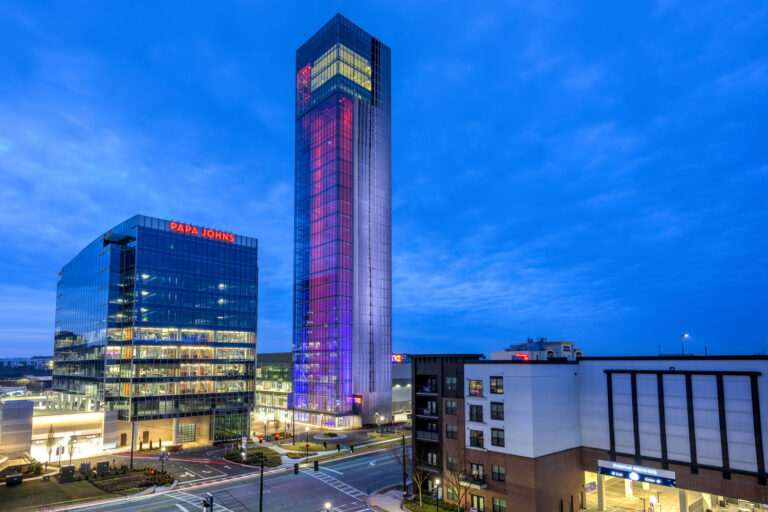 Twilight cityscape featuring illuminated TK Elevator buildings with clear branding against a dusk sky, showcasing their LEED Gold certification.