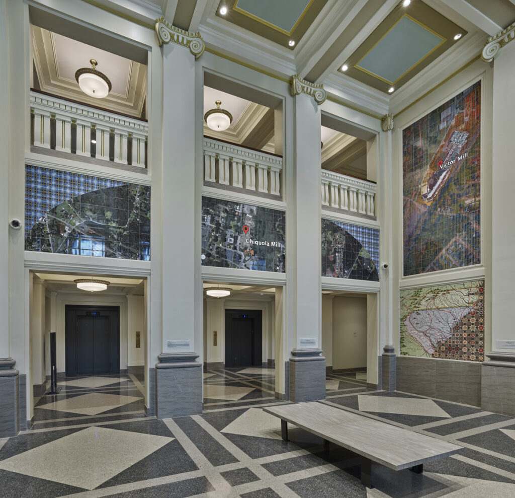 Spacious lobby with classical architecture, featuring columns, a bench, and a large wall mosaic with symbols of justice.