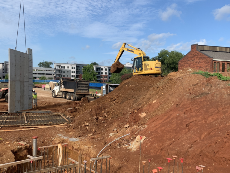 An excavator loading dirt into a dump truck at the Federal Courthouse Construction site in Huntsville Alabama with building foundations in progress.