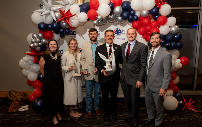 Group of professionals posing with awards for Project of the Year in front of a patriotic balloon arch at a formal event.