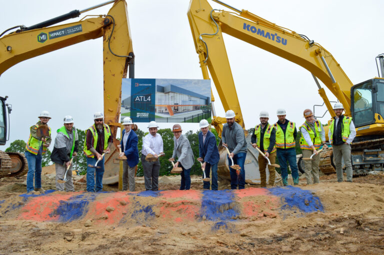 Group of individuals in hard hats and high-visibility vests at a groundbreaking ceremony for the Campus Data Center with shovels and construction equipment.