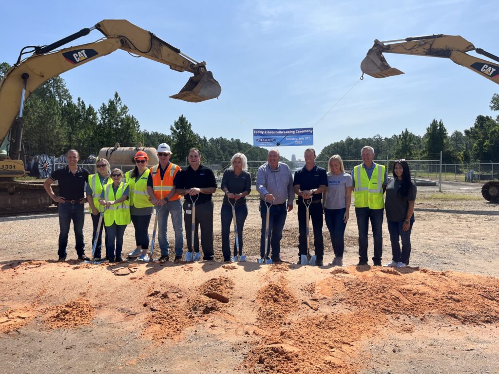 Group of individuals wearing hard hats at a groundbreaking ceremony for the Chart Manufacturing Facility in Theodore, Alabama, with excavators in the background.