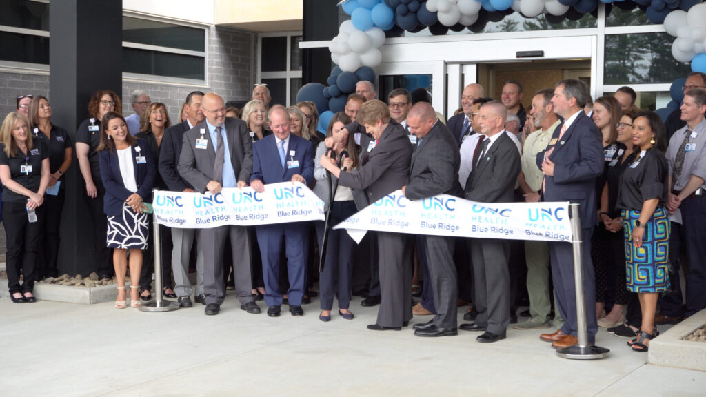 Group of individuals participating in a ribbon-cutting ceremony for the opening of the UNC Health Blue Ridge Cancer Center.