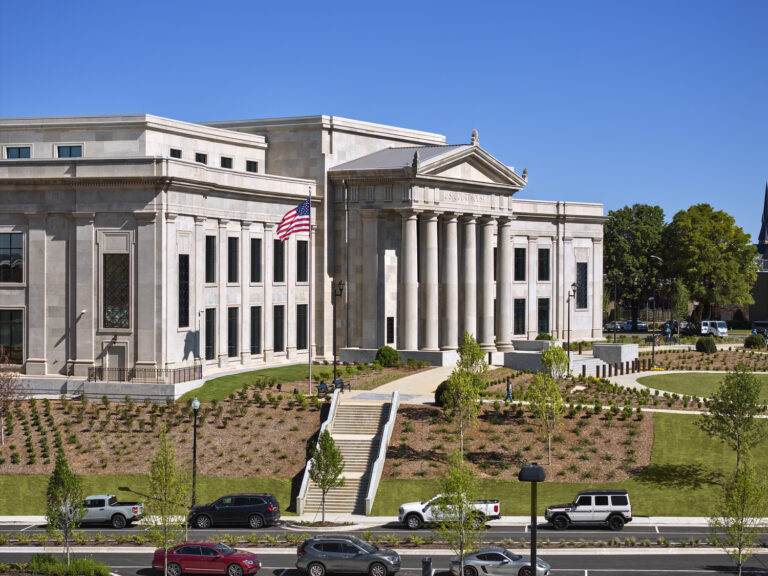 Large, white stone government building with columns, American flag, landscaped grounds, and cars parked along the street under a clear blue sky—an impressive example of the enduring quality seen in Brasfield and Gorrie government projects.