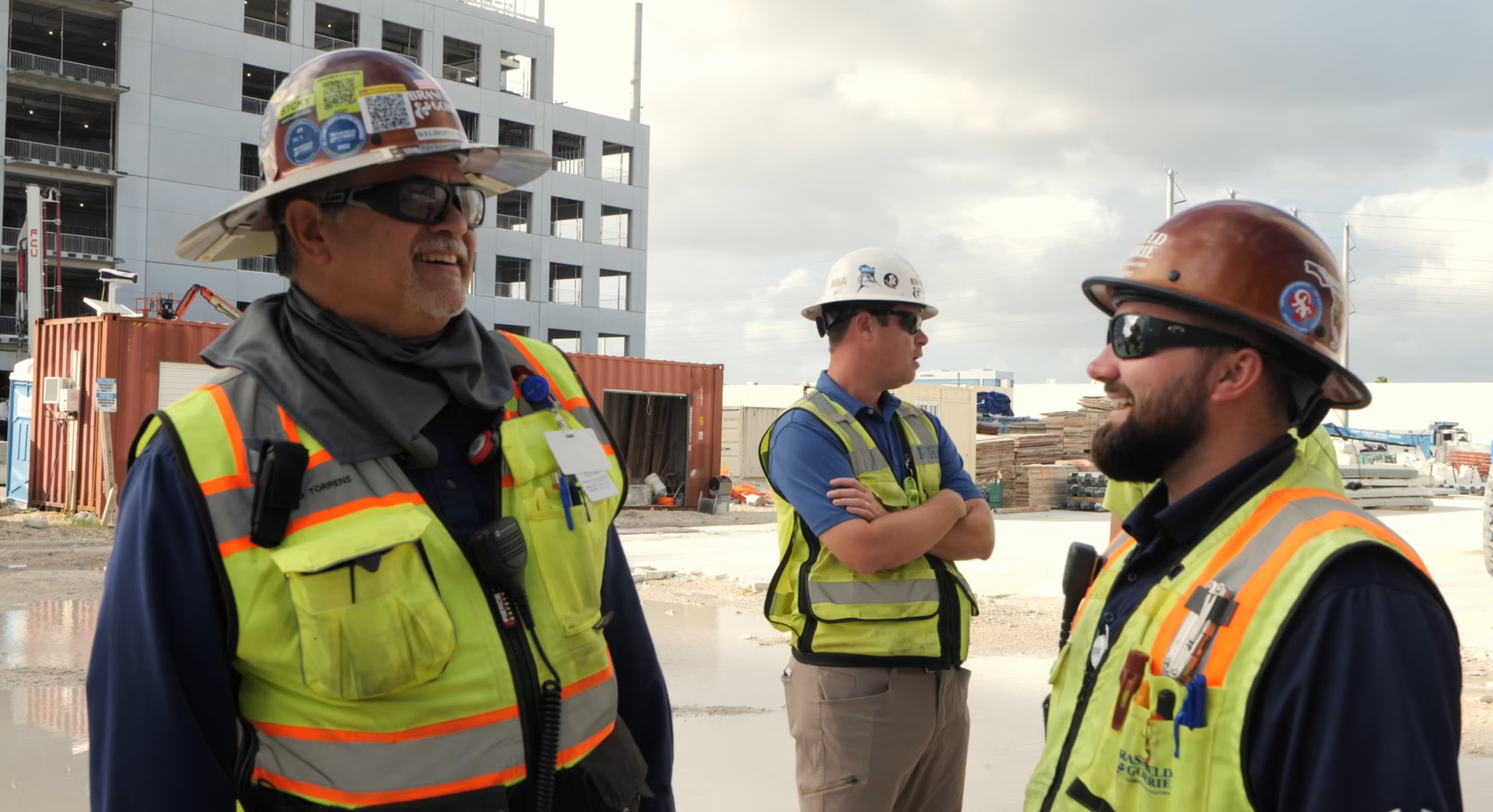 Three construction workers in safety gear discuss employment opportunities on site.