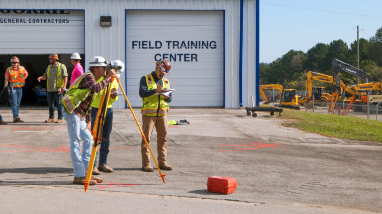 A group of construction workers standing in front of a building, taking field measurements.