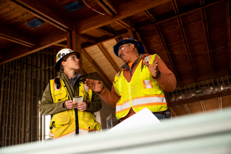Two construction workers talking in a warehouse building.