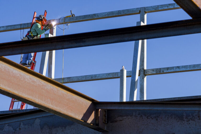 A man on a ladder working on a metal structure, welding.
