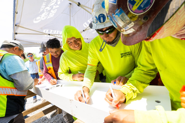 Construction workers in high-visibility clothing signing a beam at a construction site.