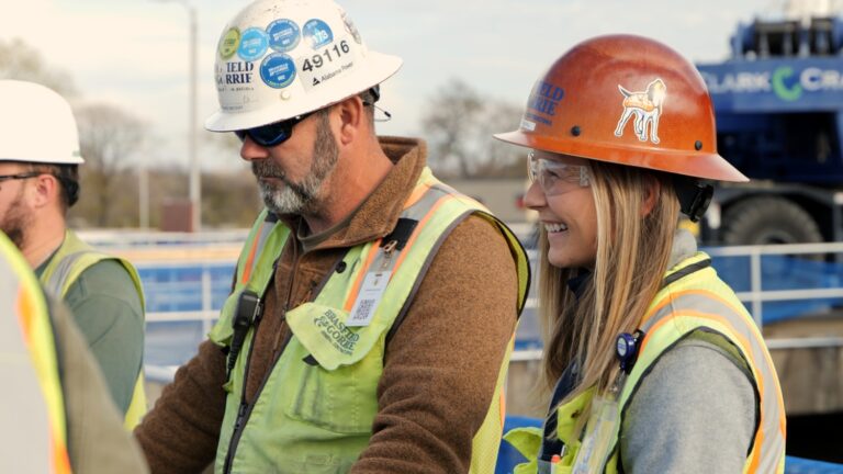 Two construction workers in hard hats and reflective vests engage in a discussion on site.