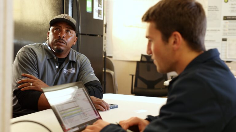 Two men engaged in a conversation at a workspace.