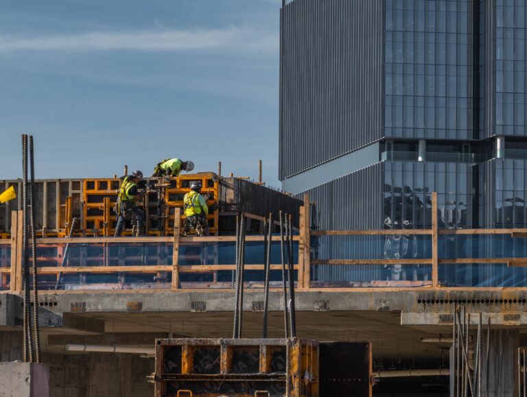 Construction workers engaging in building activities on a construction site with modern buildings in the background.