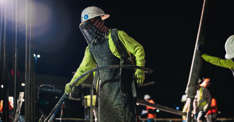 Construction worker guiding a concrete hose during a nighttime concrete pour.
