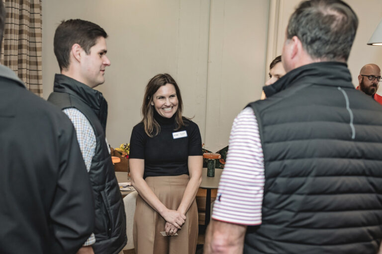 A group of people stand in the Huntsville Office of Brasfield and Gorrie having a conversation. A woman in the center smiles while talking to three men, with another person visible in the background.