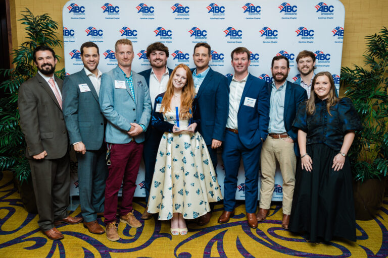 Ten people pose in front of an ABC Step Up background; one woman from the Charlotte Office of Brasfield and Gorrie stands in the center holding an award, with everyone dressed in formal or business attire.