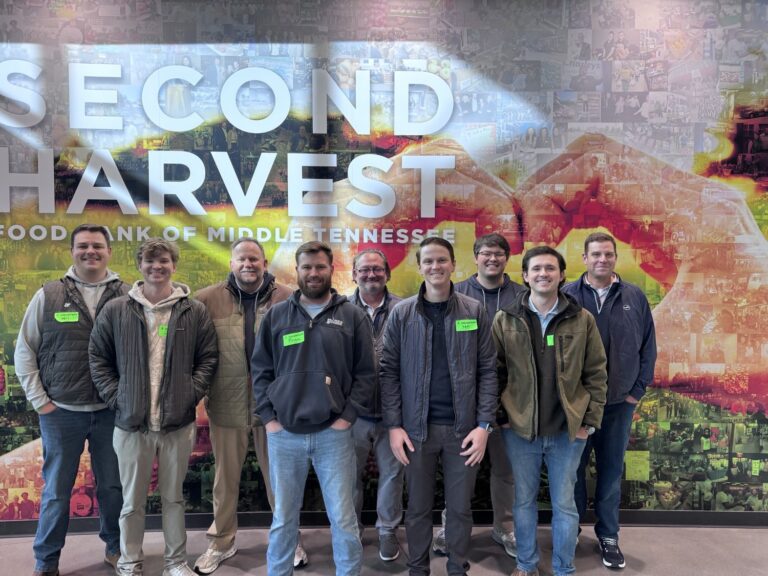 Eight men from the Nashville office of Brasfield and Gorrie stand in a line in front of a Second Harvest Food Bank of Middle Tennessee mural.