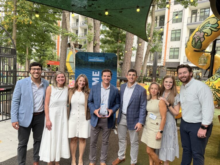 Eight people pose for a group photo at the Brasfield and Gorrie Atlanta office, with one man in the center holding a glass award in front of an Atlanta Business Chronicle banner.