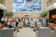 A large group poses in the Nashville office of Brasfield and Gorrie with a Chick-fil-A cow mascot in the center and a large digital screen on the back wall.