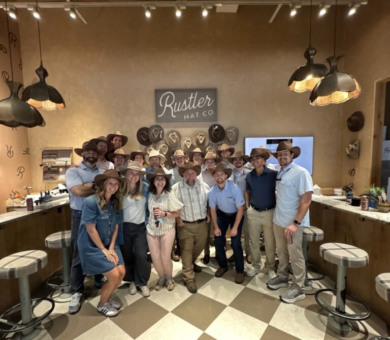 A large group of people from the Nashville office of Brasfield and Gorrie wear cowboy hats while standing in a store branded “Rustler Hat Co.”