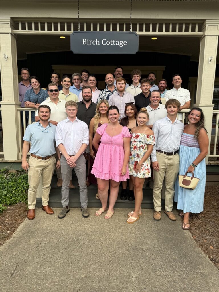 A large group of young adults from the Brasfield and Gorrie Nashville office posing for a photo on the porch of a building with a sign that reads “Birch Cottage.”