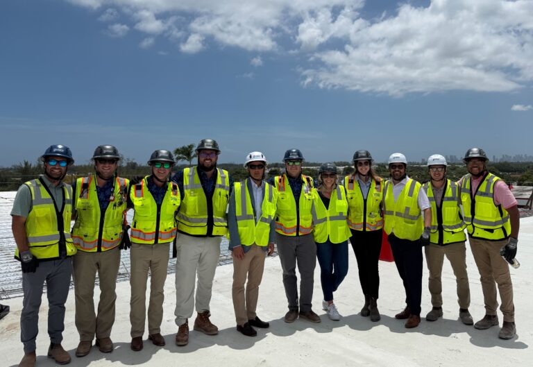 Un grupo de once personas, con cascos y chalecos de seguridad, posa al aire libre en una obra, bajo un cielo parcialmente nublado, en representación de la oficina de Miami de Brasfield and Gorrie.