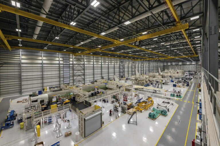 The inside of a large factory with many machines assembling planes.