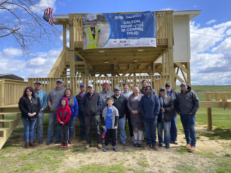 Group of people posing in front of a newly constructed wooden structure with a banner that reads 