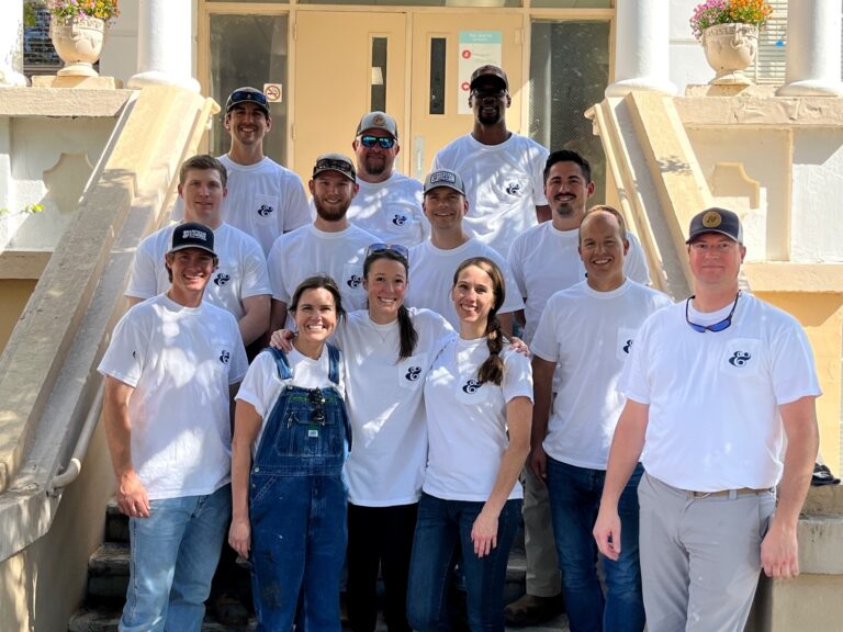 A group of smiling volunteers wearing matching t-shirts posing for a photo on a staircase.