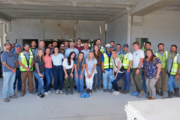 Un grupo de obreros de la construcción y el personal de la oficina de Jacksonville de Brasfield and Gorrie posan juntos para una foto de grupo en el interior de un edificio sin terminar.
