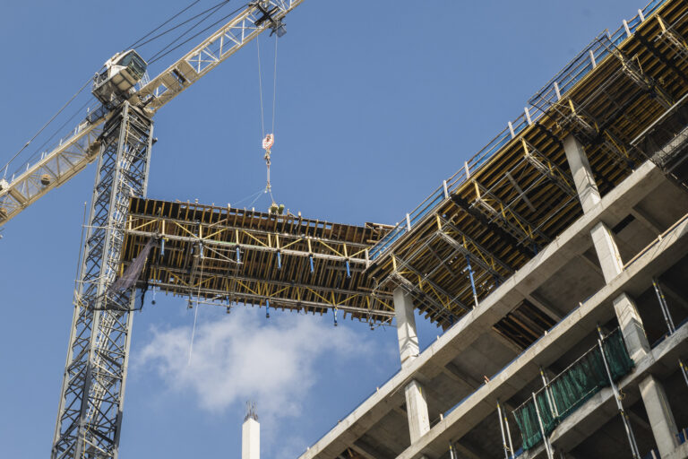 Construction crane lifting a structure segment at a building site with a clear blue sky in the background.