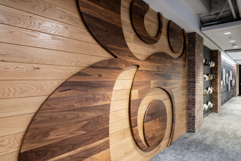 Una pared de madera con una incrustación geométrica en forma de remolino en la oficina de Brasfield and Gorrie en Charlotte, situada junto a una columna de ladrillo y un pasillo con cascos de seguridad colgados en la pared.
