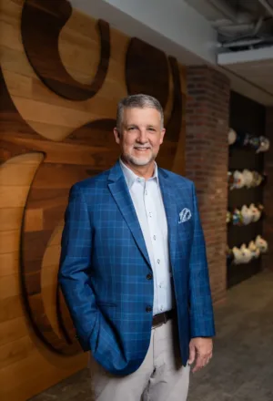 Michael Byrd, in a blue plaid jacket and khaki pants, stands indoors smiling, with a wood and brick wall in the background.