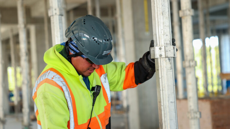 Construction worker holding metal framing on a construction site while wearing a hard hat.