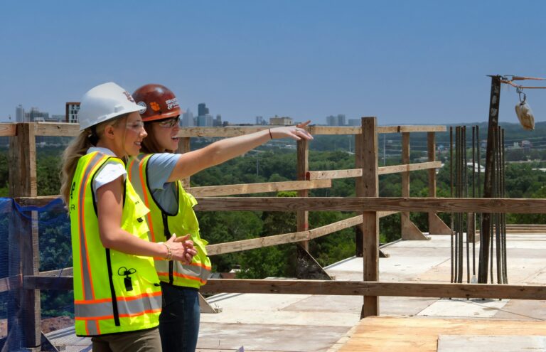 Two construction workers in safety gear discussing employment opportunities on a construction site.