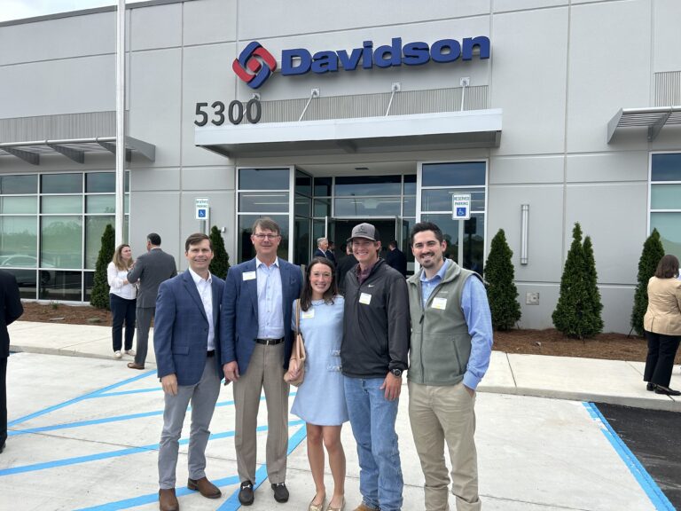 Five people posing in front of the Davidson headquarters, a gray commercial building.