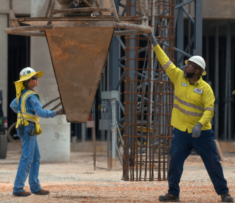 Two construction workers on their job guiding a concrete bucket at a construction site.