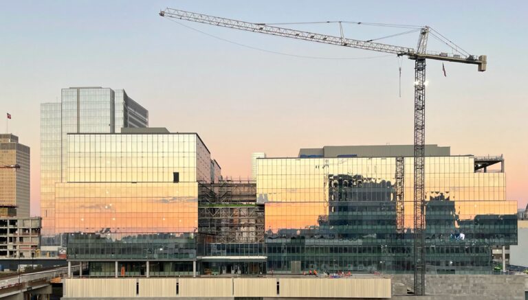 Puesta de sol reflejada en edificios de cristal en un paisaje urbano, con una grúa de construcción destacada contra el cielo, inspirando ideas para el diseño de interiores.
