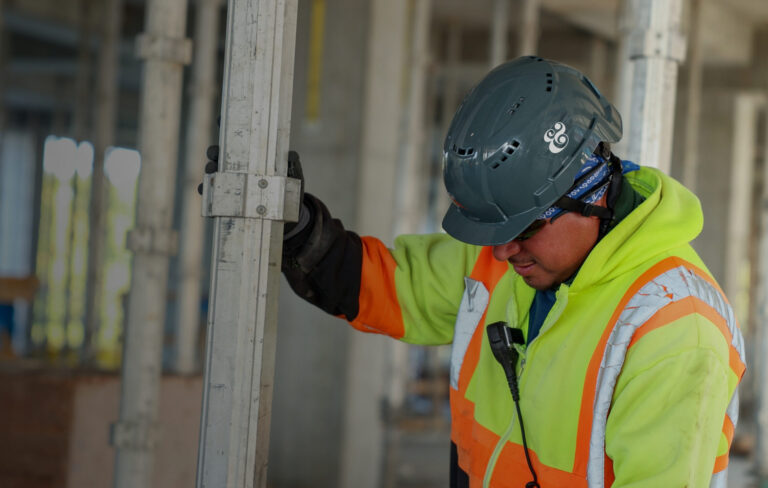Construction safety worker in gear installing a metal frame at a building site.