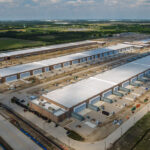Aerial view of a large industrial complex under construction in Texas, featuring multiple long warehouse buildings and surrounding areas with construction equipment.