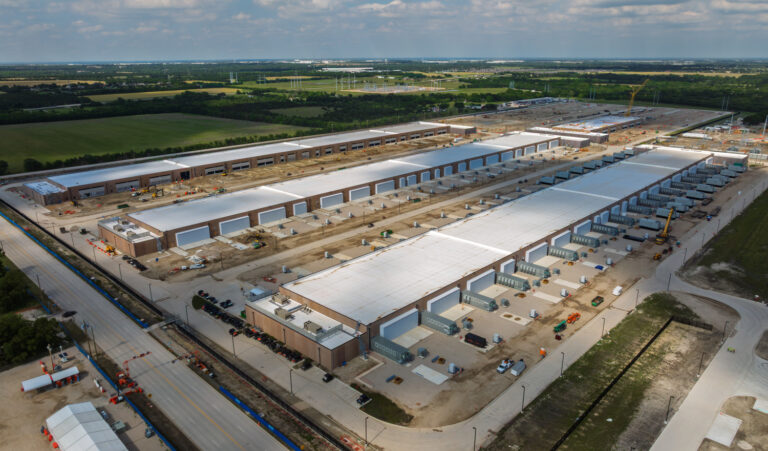 Aerial view of a large industrial complex under construction in Texas, featuring multiple long warehouse buildings and surrounding areas with construction equipment.